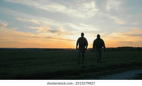 Two silhouetted soldiers walking at sunset. Ukraine Soldiers patrolling at sunset, Two soldiers walking along a rural path at dusk. - Powered by Shutterstock