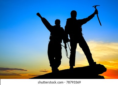 Two Silhouettes Of Climbers On The Mountain Top