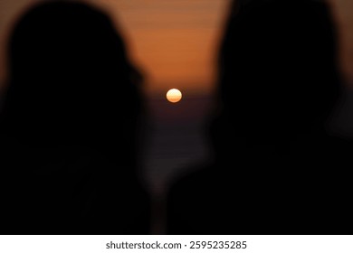 two silhouettes framing the setting sun, a moment of quiet beauty and shared contemplation