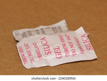 Two Silica gel packets isolated in a cardboard box. Porous desiccant substance used in packing material to absorb humidity moisture. - Shutterstock ID 2240100965
