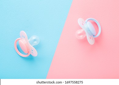 Two silicone baby soothers. Pastel pink blue table background. Closeup. First girls and boys toy.