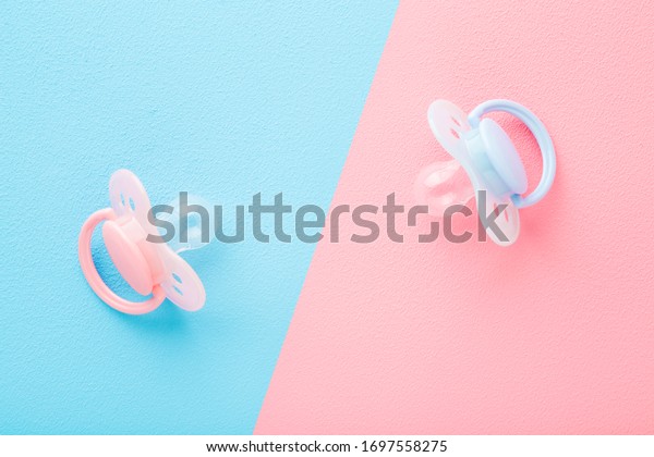 Two silicone baby soothers.\
Pastel pink blue table background. Closeup. First girls and boys\
toy.