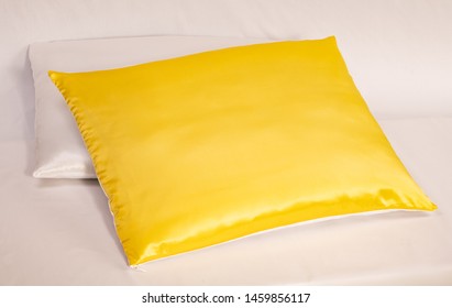 Two Silky Case Pillows Laying On A White Bed. Yellow Silky Pillow And White Silky Pillow.