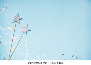Two silver party magic wands and scattered sequins on a blue background. Copy space. 