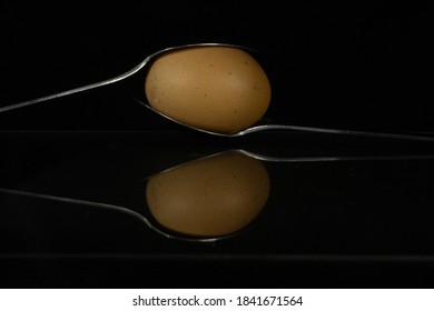 two silver table spoons with a balanced egg reflected and isolated on a black background
