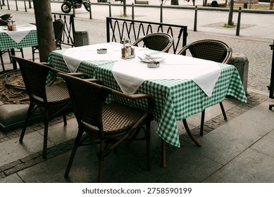 Two simple cafe tables by the sidewalk, framed by trees and iron railing, where conversations feel as natural as the passing breeze