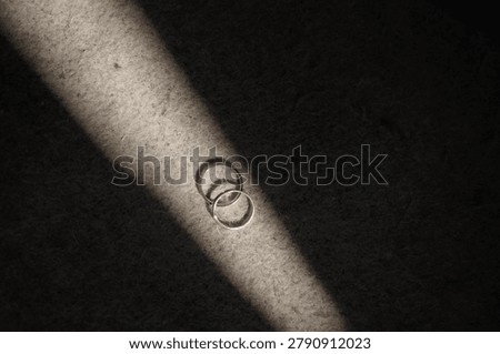 Two simple silver wedding rings in dynamic shadow ray on textured fabric background closeup