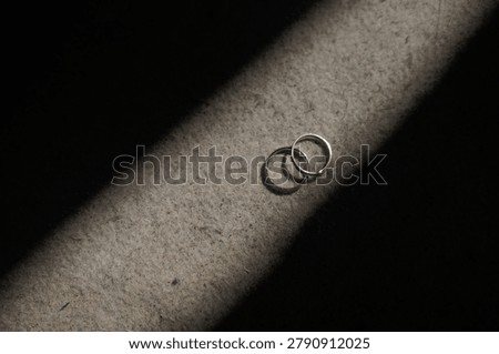 Two simple silver wedding rings in dynamic shadow ray on textured fabric background closeup