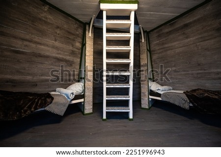 Two single beds with linen mounted in niches of a room. Pyramid shape bungalow summer house. Angled surrounded walls, white stairs, gray horizontal wooden wall planks. Nonstandard frame construction.