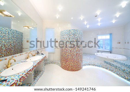 Two sinks and big mirror in spacious bathroom with jacuzzi and blue and red tiles.