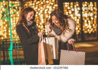 Two Sisters Enjoy The Night In Shopping And Laughing With Shopping Bags In Their Hands.