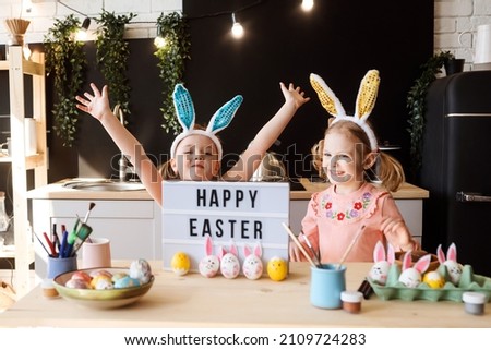 Two sisters are having fun while decorating Easter eggs at the kitchen, happy Easter congratulation. One girl is in motion, selective focus. 
