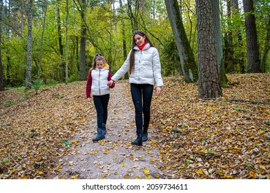 Two Sisters Holding Hands, Dressed In Light Jackets, Walking In The Forest In Autumn