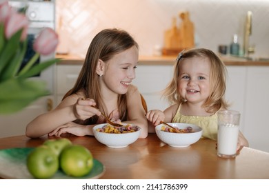 two sisters in pajamas having breakfast in the kitchen eating colorful cereal with milk at home in the morning