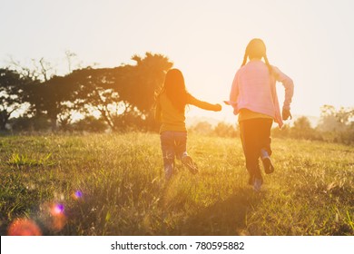 Two Sisters Running On The Lawn In The City Park Outdoor. Freedom And Carefree. Happy Childhood. Happy Children Running Around Outside Playing Catch-up Concept