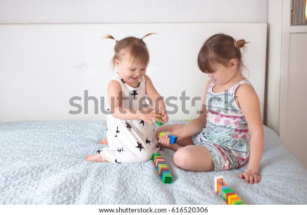 two sisters siblings  laugh play in the\
constructor, build a tower on a light background in real interior.\
The concept of mutual aid and the\
relationship
