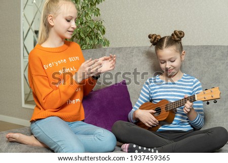 Two sisters sitting on ground floor,play ukulele with interested feeling,doing activity together