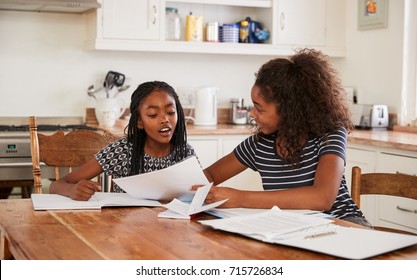 Two Sisters Sitting At Table In Kitchen Doing Homework - Powered by Shutterstock