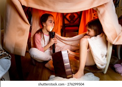 Two Sisters Telling Scary Stories Under Blanket At Night