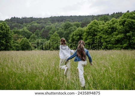 Two sisters walking at meadow through grass, having fun, exploring. Sisterly love and siblings relationship concept.
