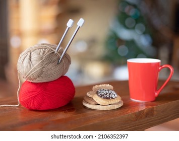 Two skeins of thread with knitting needles on a wooden table with a mug of tea and cookies.