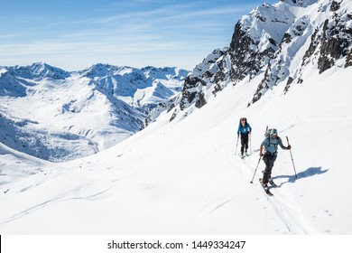 Two skiers skinning uphill on a hot sunny day in the Alaska backcountry of the Talkeetna Mountains.
