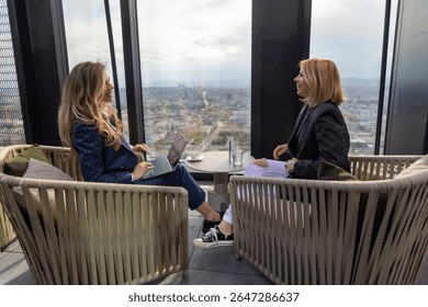 Two skilled professionals are actively engaged in a thoughtprovoking discussion while they are seated comfortably in a contemporary, stylish space that offers a stunning city skyline as a backdrop