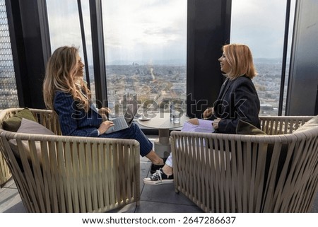 Two skilled professionals are actively engaged in a thoughtprovoking discussion while they are seated comfortably in a contemporary, stylish space that offers a stunning city skyline as a backdrop
