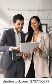 Two skilled, successful teammates using tablet in office. New Zealander woman, Middle-Eastern man in formalwear reviewing new corporate software, program or innovative business tools during meeting
