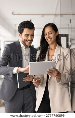 Two skilled, successful teammates using tablet in office. New Zealander woman, Middle-Eastern man in formalwear reviewing new corporate software, program or innovative business tools during meeting