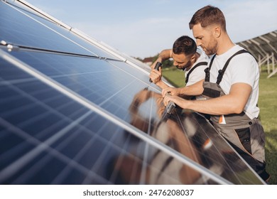 Two skilled workers or craftsmen wearing working gray uniforms, technicians are installing solar panels on a solar farm for clean energy and electricity supply - Powered by Shutterstock