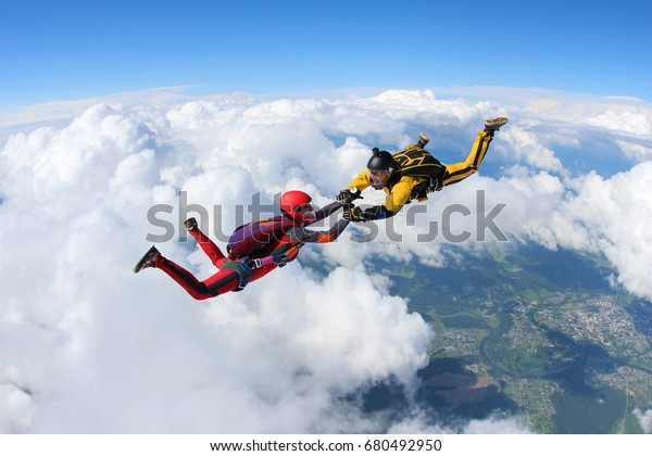 Two skydivers are falling against the background\
of the white clouds.