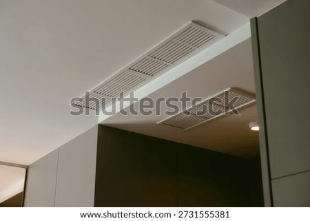 Two sleek, rectangular ventilation grilles are seamlessly integrated into a minimalist white ceiling and wall, highlighting modern interior design and climate control infrastructure.