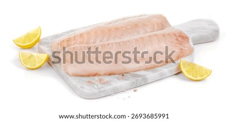 Two slices of cod on marble cutting board with lemon wedges isol