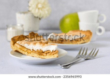 Two slices of pie with apple, cinnamon and meringue on saucers, forks and cups for coffee, a green apple and a vase with a flower.