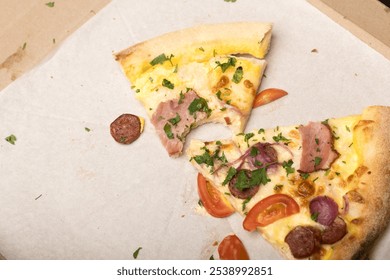 Two slices of pizza in a box on parchment paper with sausage, ham, tomato, red onion, and parsley. One slice has a bite taken out. Great for food delivery and casual dining themes. - Powered by Shutterstock