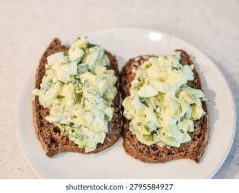 Two slices of rye bread topped with egg avocado salad on a white plate. Ready to eat and enjoy!