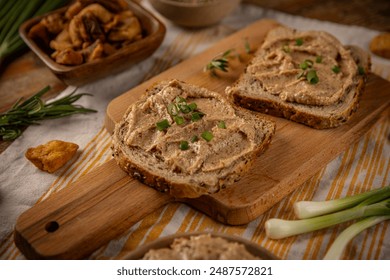 Two slices of toasted bread with spread and chives lying on wooden board, rosemary and greaves around