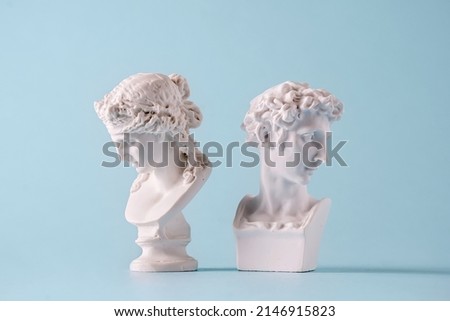 Two small antique style Roman or Grecian busts of young men facing away from each other on blue