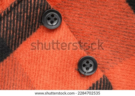 Two small black clothes buttons sewn on wool orange coat closeup