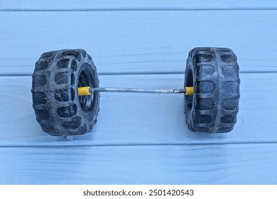 two small black plastic wheels on a thin metal axle from a toy car lie on a gray wooden table