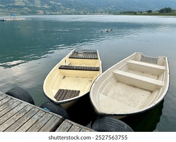 Two small boats docked on a tranquil lake with mountains nearby - Powered by Shutterstock