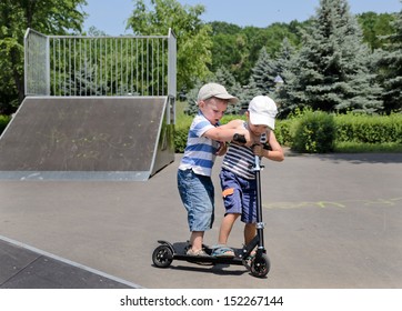 Two Small Boys Standing Arguing And Fighting Over Who Will Get To Ride A Scooter In The Skate Park