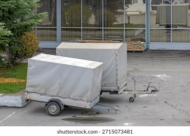 Two Small Cargo Trailers With Grey Canopy Parked Behind Building