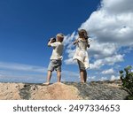 Two small children standing on a small mountaintop scouting with binoculars