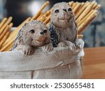 Two small figurines of hedgehogs are sitting in a white basket. The basket is filled with crackers