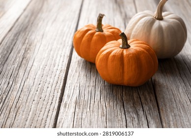 Two small orange pumpkins and one white pumpkin arranged on a textured weathered wooden table