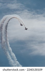two small planes fly in parallel describing a white trajectory over the blue sky. condensation trails. synchronization of concepts and association.