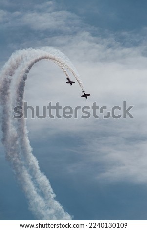 two small planes fly in parallel describing a white trajectory over the blue sky. condensation trails. synchronization of concepts and association.