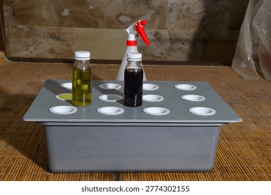 Two small plastic bottles containing yellow and dark purple liquid nutrients sit on a grey hydroponic tray with a white spray bottle behind it, arranged on a bamboo mat for indoor gardening.